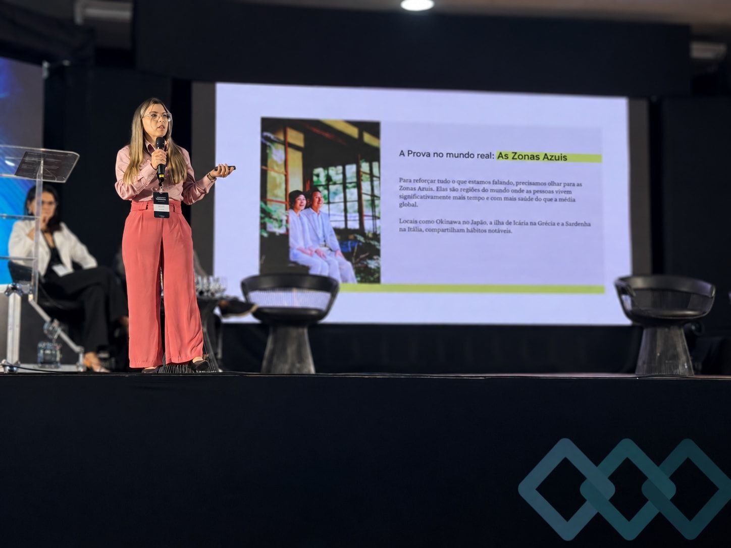 Dra. Josy Dantas no palco, falando ao microfone para uma plateia